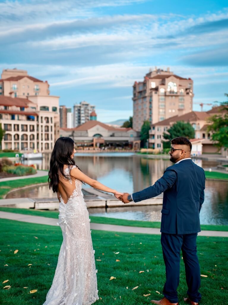 Couple holding hands on waterfront grass with city behind, Kelowna couple photoshoot